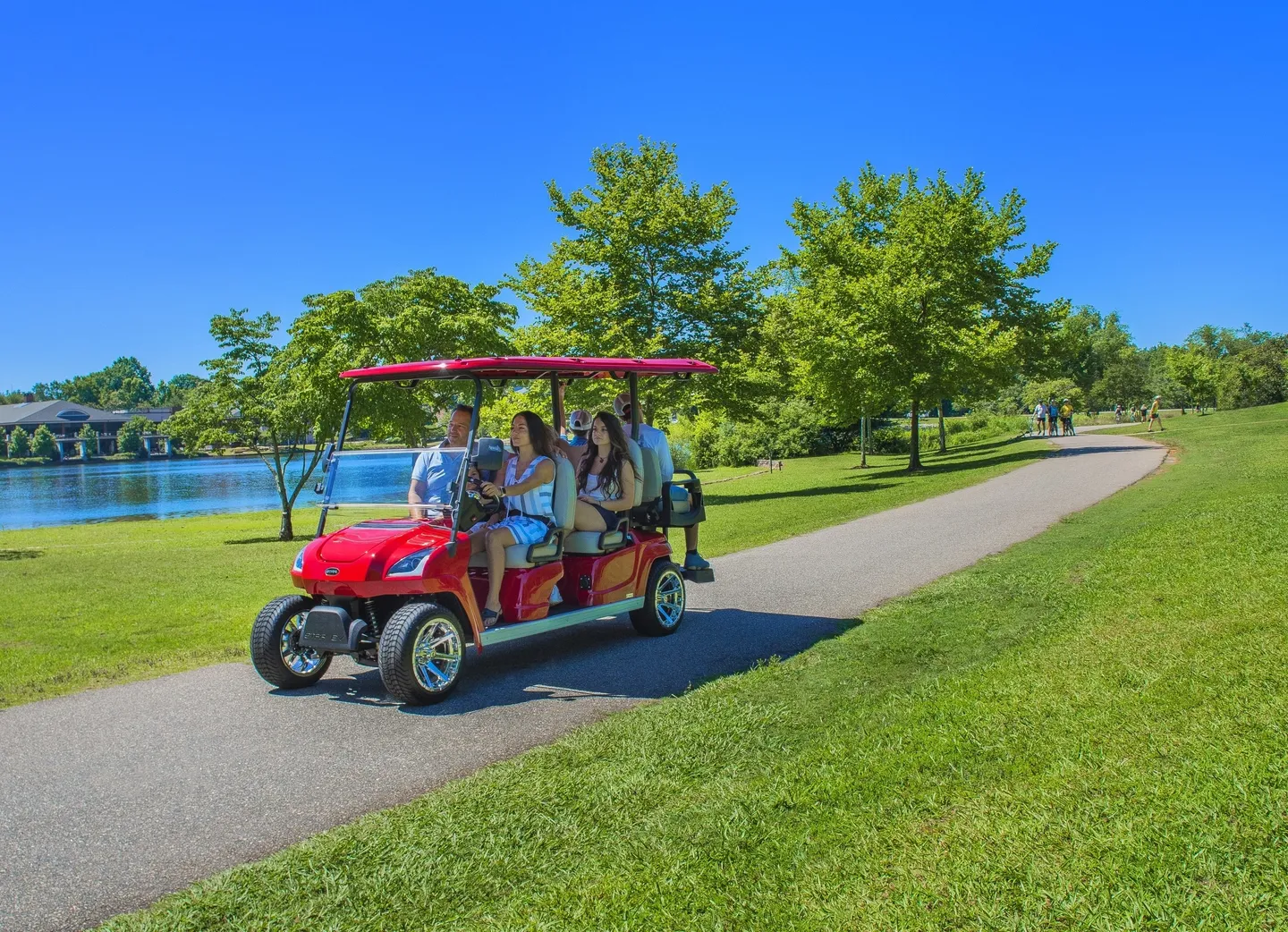 A group riding a red golf cart on a sunny day in a park.