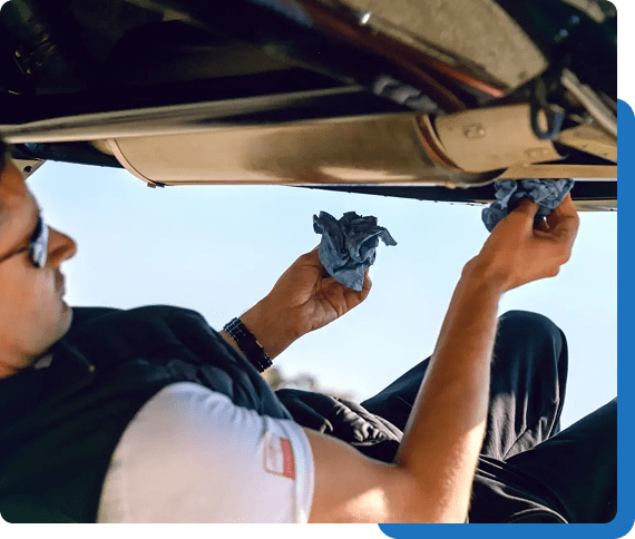 A man fixing a car part under the hood on a sunny day.