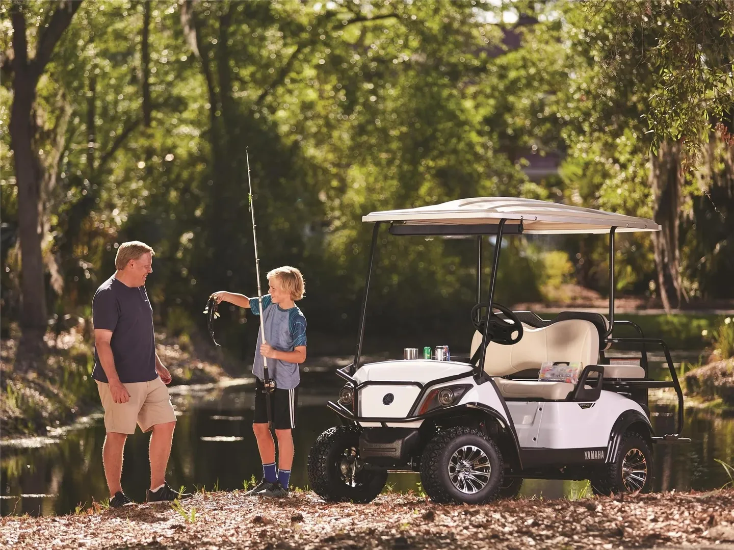 A father and son prepare to fish beside a golf cart in a wooded area.