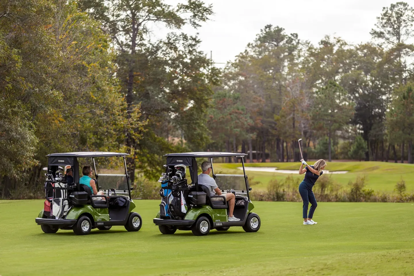 Golfers playing on a lush green course with golf carts nearby.